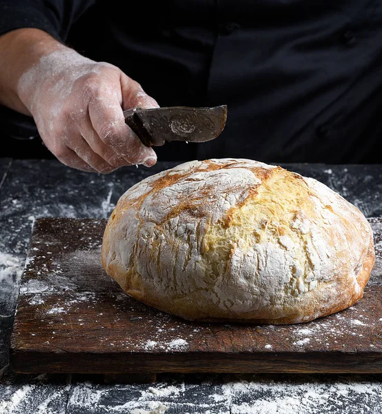 Mão Chef Masculino Segura Faca Sobre Pão Assado Redondo Inteiro — Fotografia de Stock