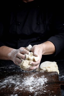 Baker beyaz buğday unu hamur kahverengi ahşap bir masa üzerinde kneads
