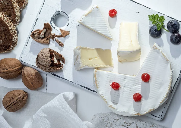 丸いカマンベール チーズ スライス ホワイト木製ボード 白い木製のテーブル トップ ビュー — ストック写真