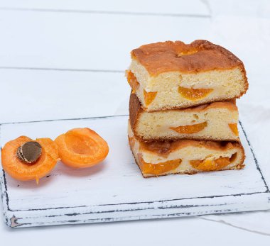 kare dilimler beyaz ahşap bir masa üzerinde kayısı ile bisküvi pastası yığını pişmiş, yakın çekim