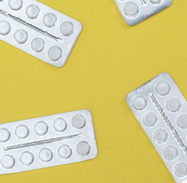 bir paket içinde farklı beyaz tabletler sarı bir arka plan üzerinde üstten görünüm dağılmış