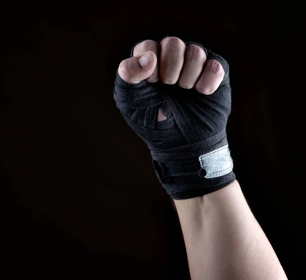 male  hand is wrapped in a black sports textile bandage on a black background, copy space