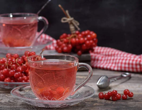 hot viburnum tea in a transparent cup with a handle and saucer on a gray wooden table, next to fresh berries