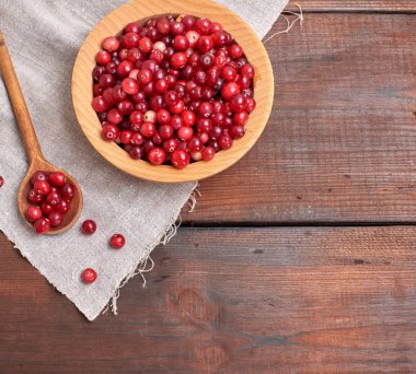Olgun lingonberries beyaz bir tabloda, üstten görünüm ahşap bir kase kırmızı meyveler