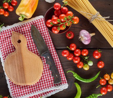 Uzun, çiğ bir spagetti demetinin yanında bıçak ve taze kiraz domatesleri ile tahta kesmek.