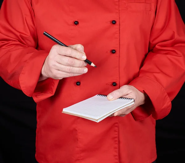 Chef Uniforme Vermelho Segurando Caderno Branco Lápis Madeira Preto Fundo — Fotografia de Stock
