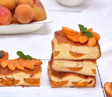 Beyaz ahşap bir tahtada taze kayısıları olan kare şeklinde kek süngerleri.