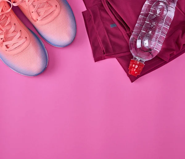 kadın spor ayakkabı ve bir su şişesi üzerinde pembe bir arka plan, üstten görünüm