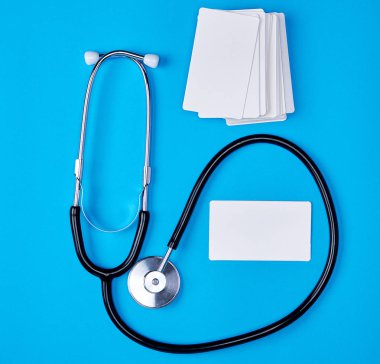 Tıbbi steteskop ve mavi arka planda boş kağıt kartvizitler.