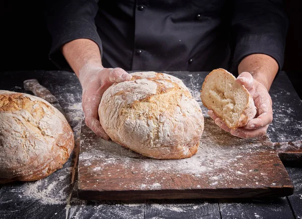 Cozinhe em uma túnica preta mantém pão cozido no forno fresco — Fotografia de Stock