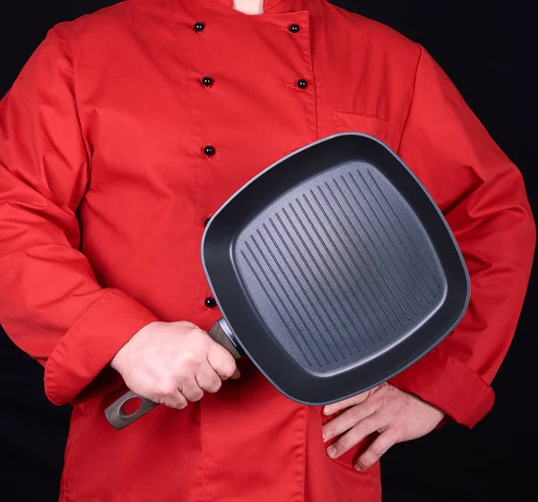 Cozinhe em uniforme vermelho segurando uma frigideira preta quadrada vazia — Fotografia de Stock