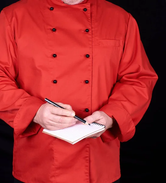 Chef de uniforme vermelho segurando um caderno em branco e um preto de madeira — Fotografia de Stock