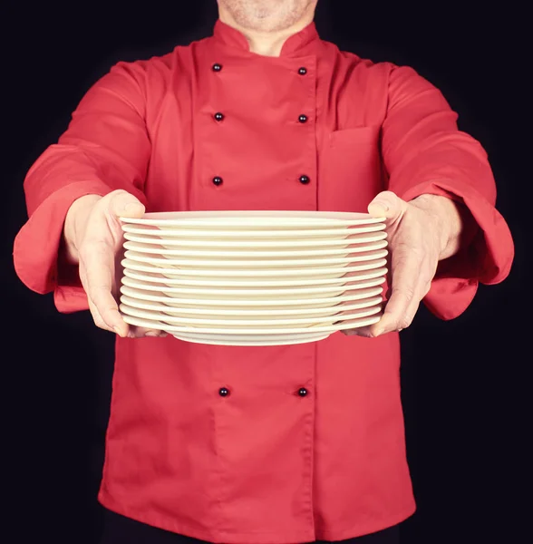 Cozinhe em uniforme vermelho segura em suas mãos uma pilha de redondo branco em — Fotografia de Stock