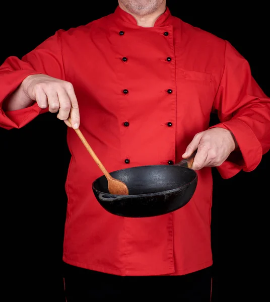 Cozinhar em uniforme vermelho segurando uma frigideira preta vazia e woode — Fotografia de Stock