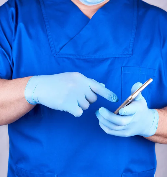 Arzt in blauer Uniform und Latexhandschuhen hält ein Handy in der Hand — Stockfoto