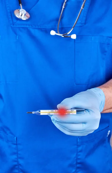 Doctor en uniforme azul y guantes de látex viejos que sostienen un th médico —  Fotos de Stock