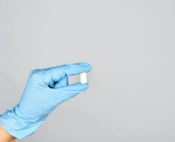 Mão luva estéril azul segurando uma pílula branca — Fotografia de Stock
