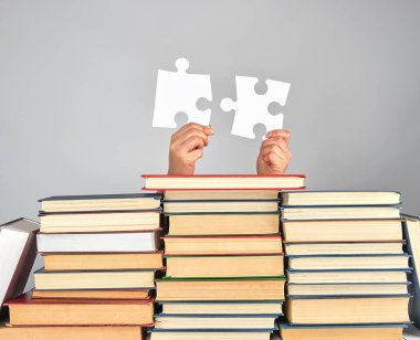 bir kitap yığını üzerinde büyük beyaz bulmaca tutan kadın eller