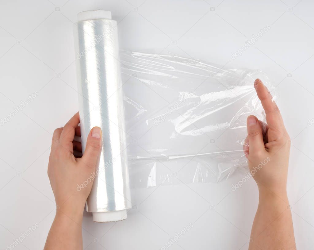 two hands hold a large roll of wound white transparent film for 