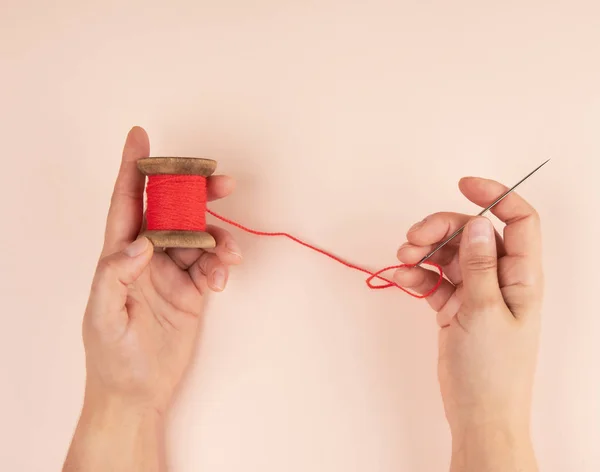 two hands hold a wooden bobbin with red wool threads