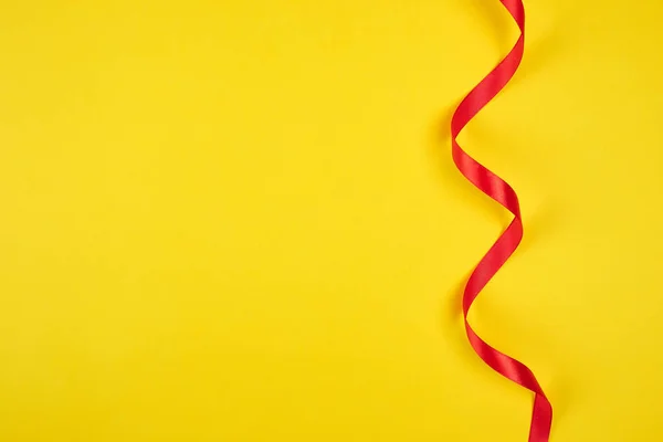 Bükülmüş kırmızı ipek kurdele, sarı arka plan — Stok fotoğraf