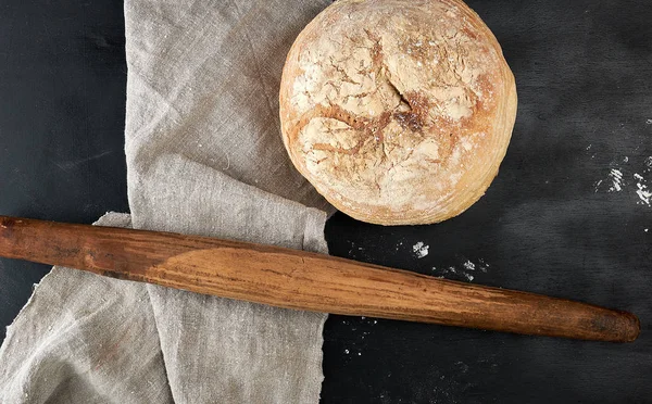 Круглый хлеб и деревянная старая скалка на черном столе — стоковое фото