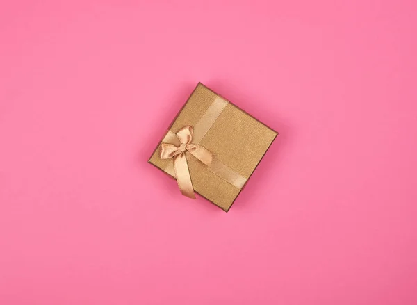 ピンクの背景に弓を持つ閉じた金色のギフトボックス — ストック写真