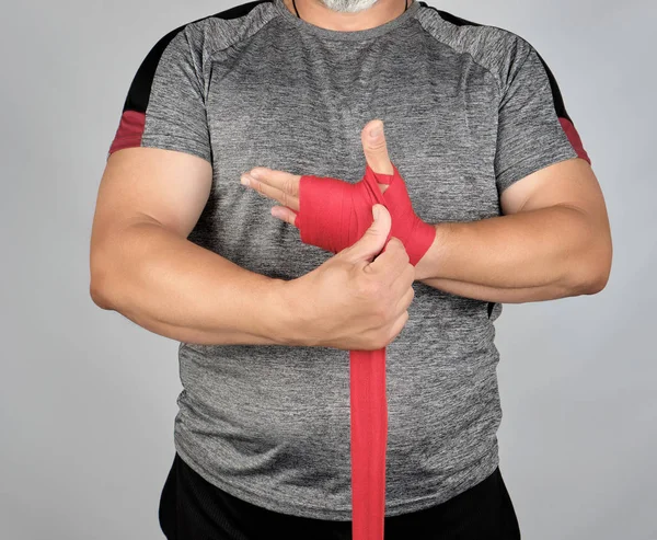 Atlet berdiri dalam pakaian abu-abu dan membungkus tangannya dalam tekstil merah — Stok Foto