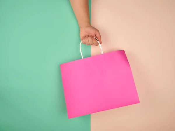 Mão feminina segurando um saco de compras de papel rosa no bac bege verde — Fotografia de Stock