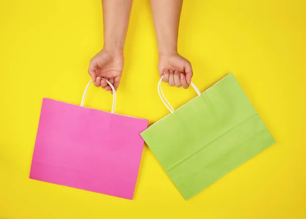 黄色の背景に紙の買い物袋を保持する2つの手 — ストック写真