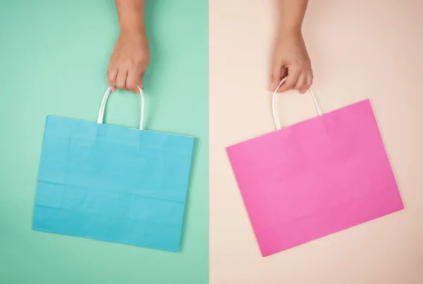 Dos manos sosteniendo bolsas de compras de papel en fondo de color abstracto — Foto de Stock