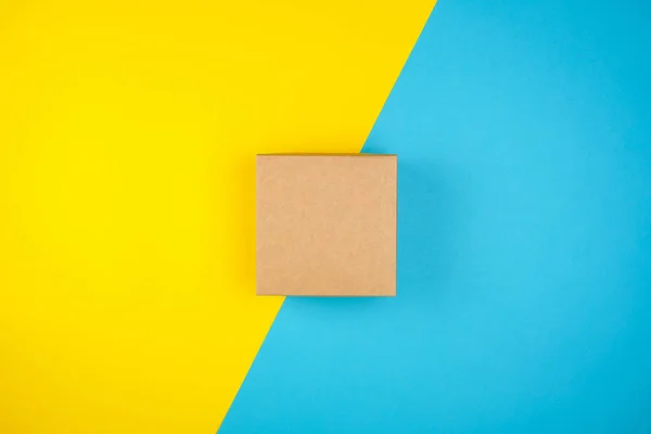 Kwadrat brązowy prezent pudełko na żółto-niebieskim tle — Zdjęcie stockowe