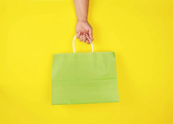 Mano femenina sosteniendo una bolsa de compras de papel verde sobre fondo amarillo — Foto de Stock