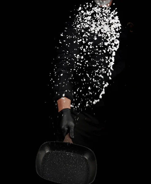 Chef en uniforme negro sostiene una sartén con sal blanca y vomita — Foto de Stock