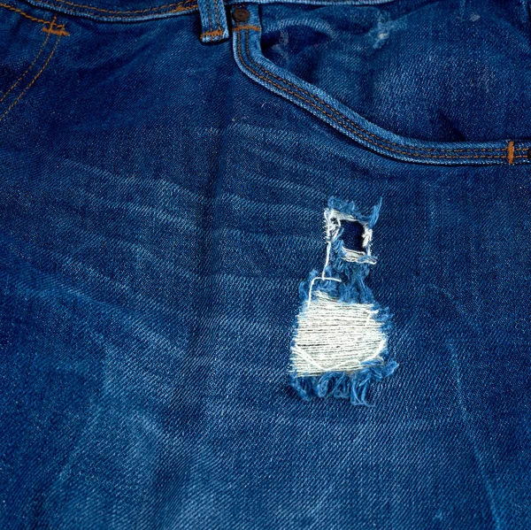 Frammento di tessuto jeans blu con un foro — Foto Stock