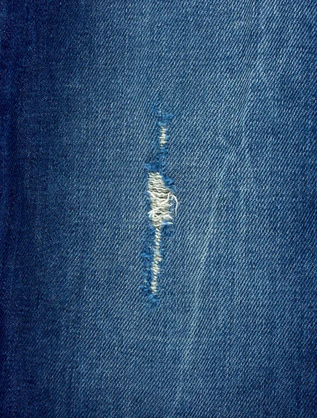 Fragment of blue jeans fabric with a hole, full frame — Stock Photo, Image