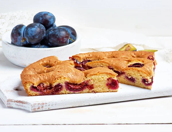 Slices of biscuit plum cake on a white wooden board and fresh fr — Stock Photo, Image