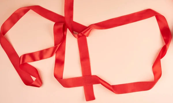 curled red satin ribbon on a beige background