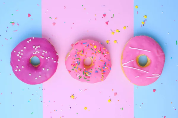 Drie ronde verschillende zoete donuts met hagelslag op een roze-blauw — Stockfoto