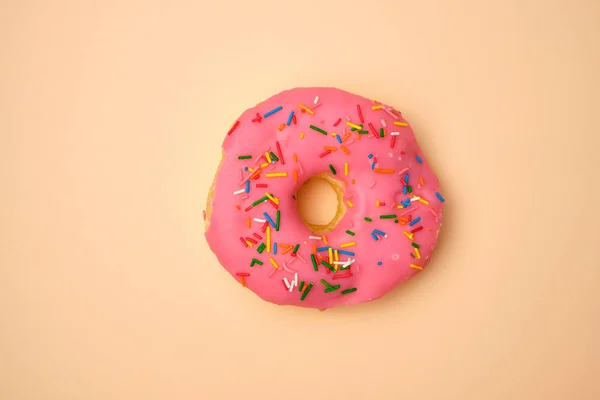 Bej bir arka plan üzerinde renkli sprinkles ile pembe yuvarlak donut — Stok fotoğraf