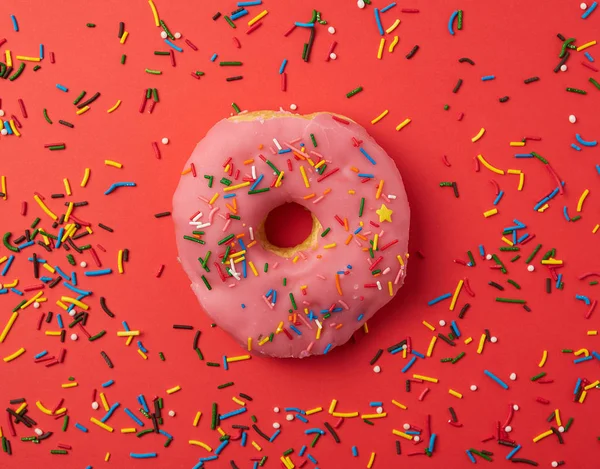 Kırmızı bir arka plan üzerinde renkli sprinkles ile bir pembe yuvarlak donut — Stok fotoğraf