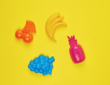 sarı bir arka planda çok renkli plastik oyuncaklar meyveler