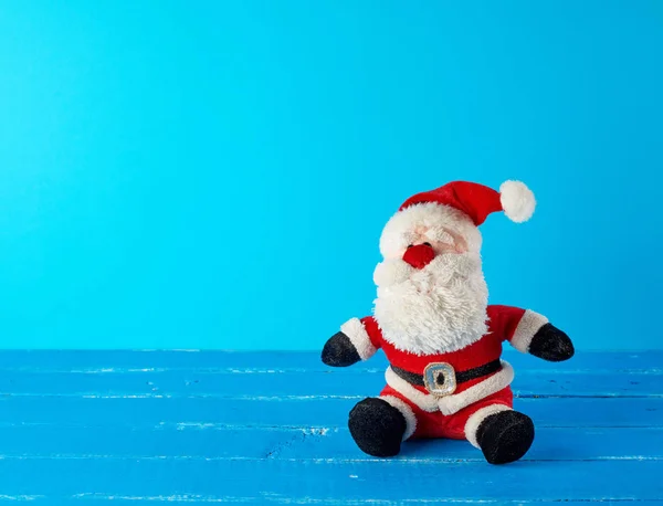Іграшка Санта Клаус у червоному костюмі, що сидить на синьому фоні — стокове фото