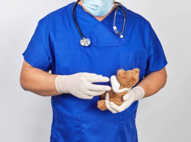 mavi üniforma ve lateks eldiven doktor kahverengi bir oyuncak ayı tutar