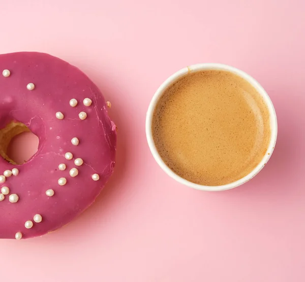 round red glazed donut and paper cup with coffee on a pink backg