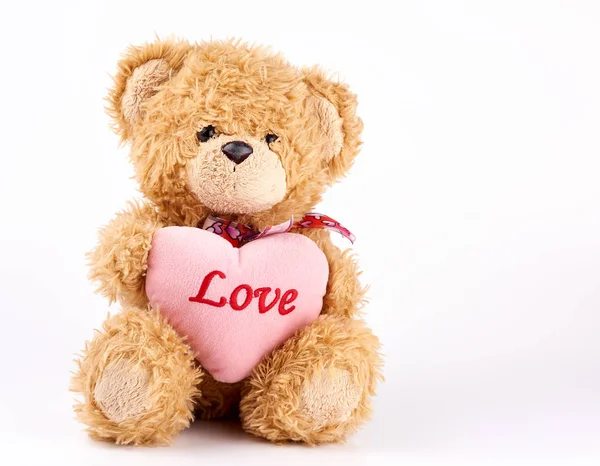 Beige teddy bear holds a pink heart, white background Stock Photo