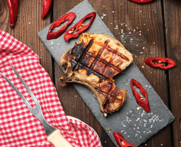 Sepotong daging babi goreng tenderloin pada tulang terletak di papan hitam — Stok Foto