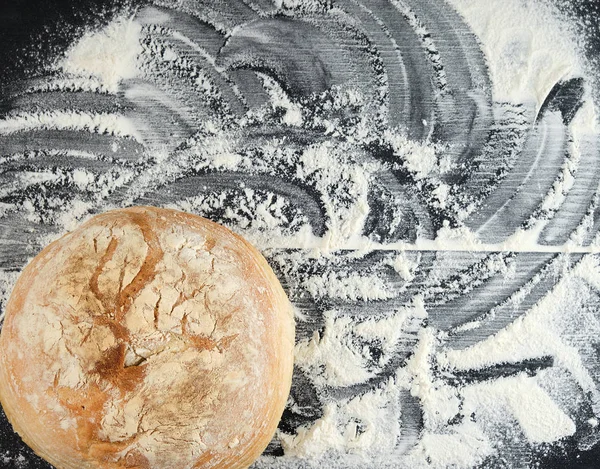 Pão assado redondo e farinha de trigo branco espalhados em uma aba preta — Fotografia de Stock