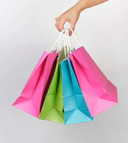 Mano femenina sosteniendo cuatro bolsas de embalaje de papel de colores — Foto de Stock