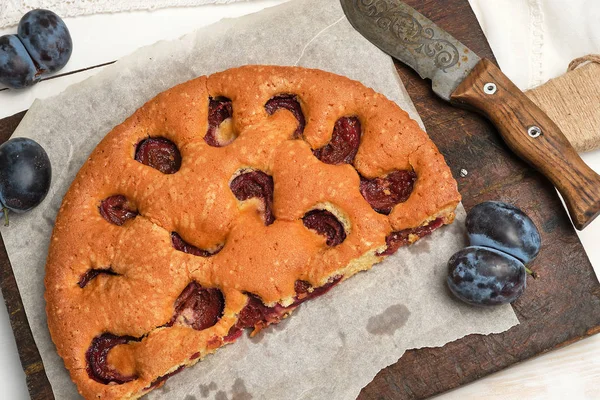 Gâteau à la prune demi-éponge sur papier parchemin et couteau, vue de dessus — Photo